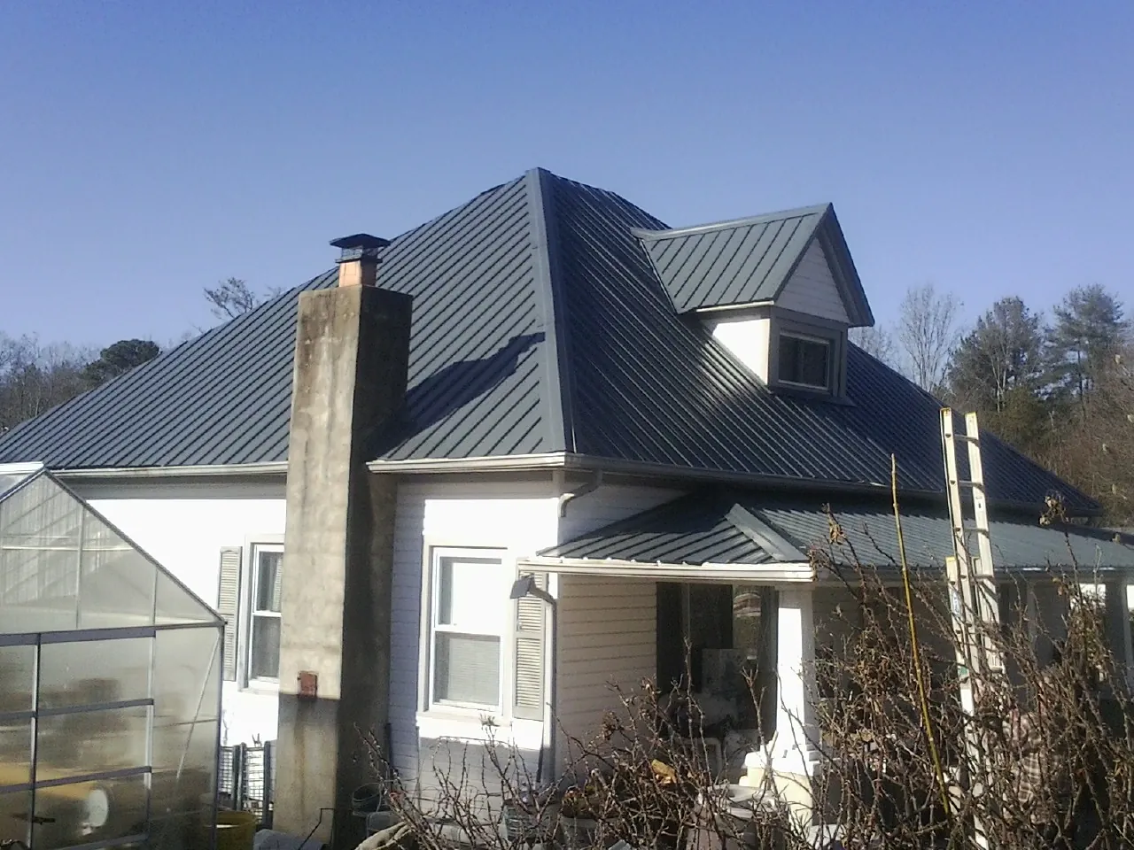 Dark blue standing seam metal roof on a white farmhouse with dormer — Slate & Tile Roof Repair by Roofing Brothers in East Dubuque