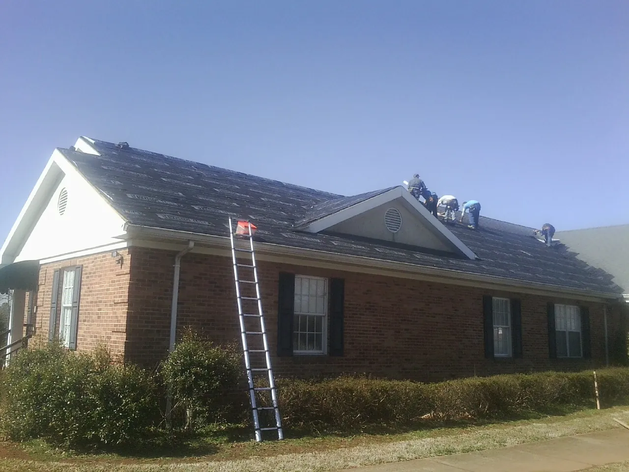 Crew tearing shingles off a brick ranch roof with a ladder set — Metal Roof Repair work by our crew in East Dubuque
