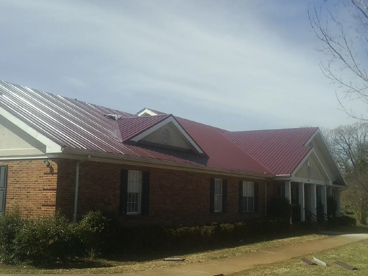 Red metal roof with gabled entries on a long brick building, from a Hail Damage Roof Repair job in East Dubuque