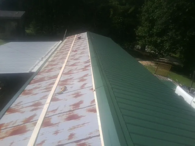 Old rusted panels beside newly installed green metal roofing — Wind Damage Roof Repair by Roofing Brothers in East Dubuque