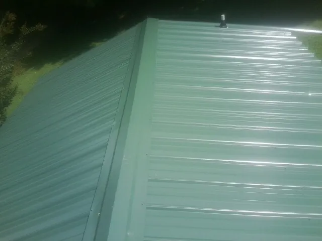 New green metal panels meeting at the ridge of a roof — Flat Roof Repair work by our crew in East Dubuque
