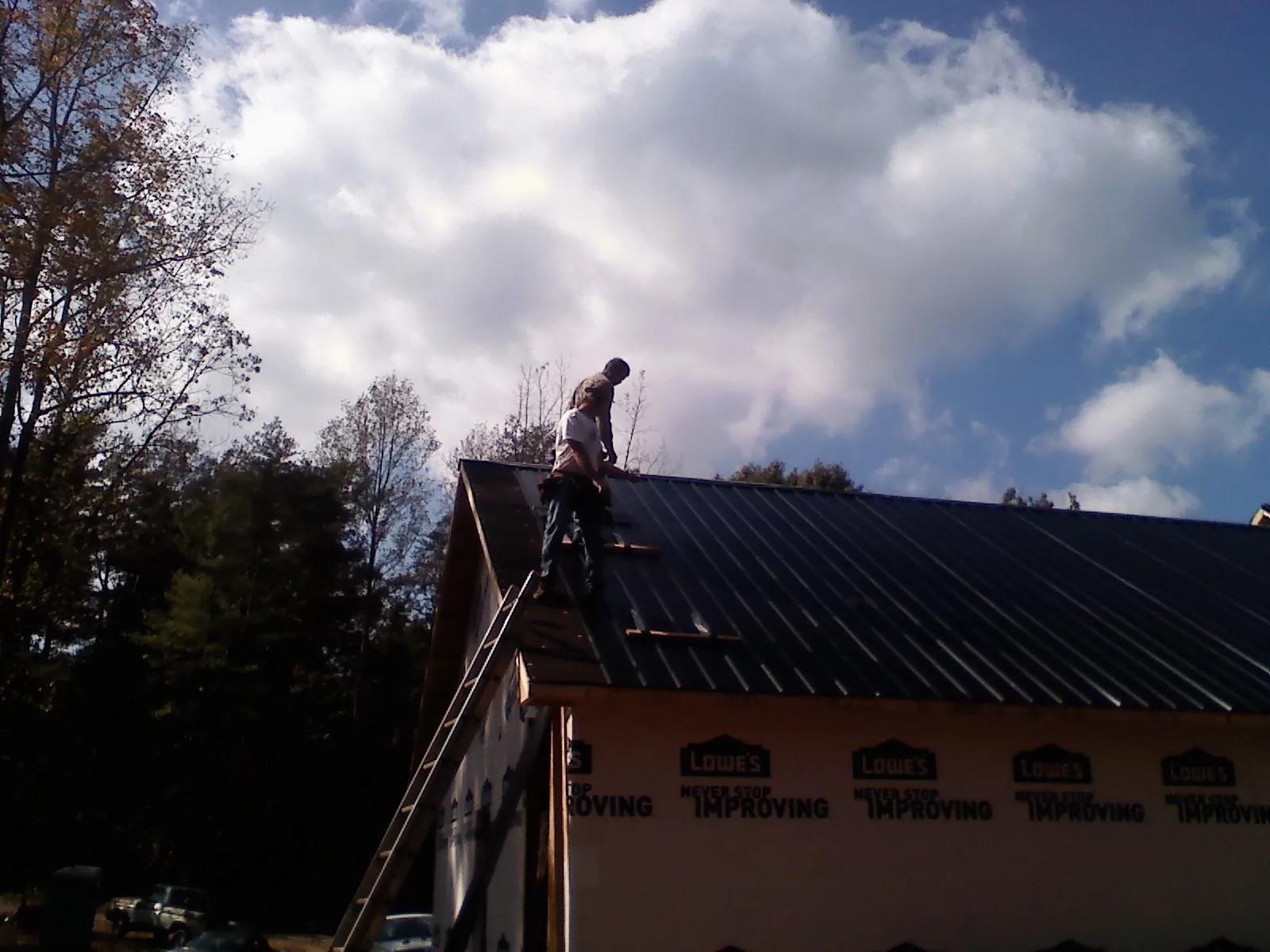 Roofer fastening dark metal panels high against a cloudy sky, from a Roof Inspection job in East Dubuque