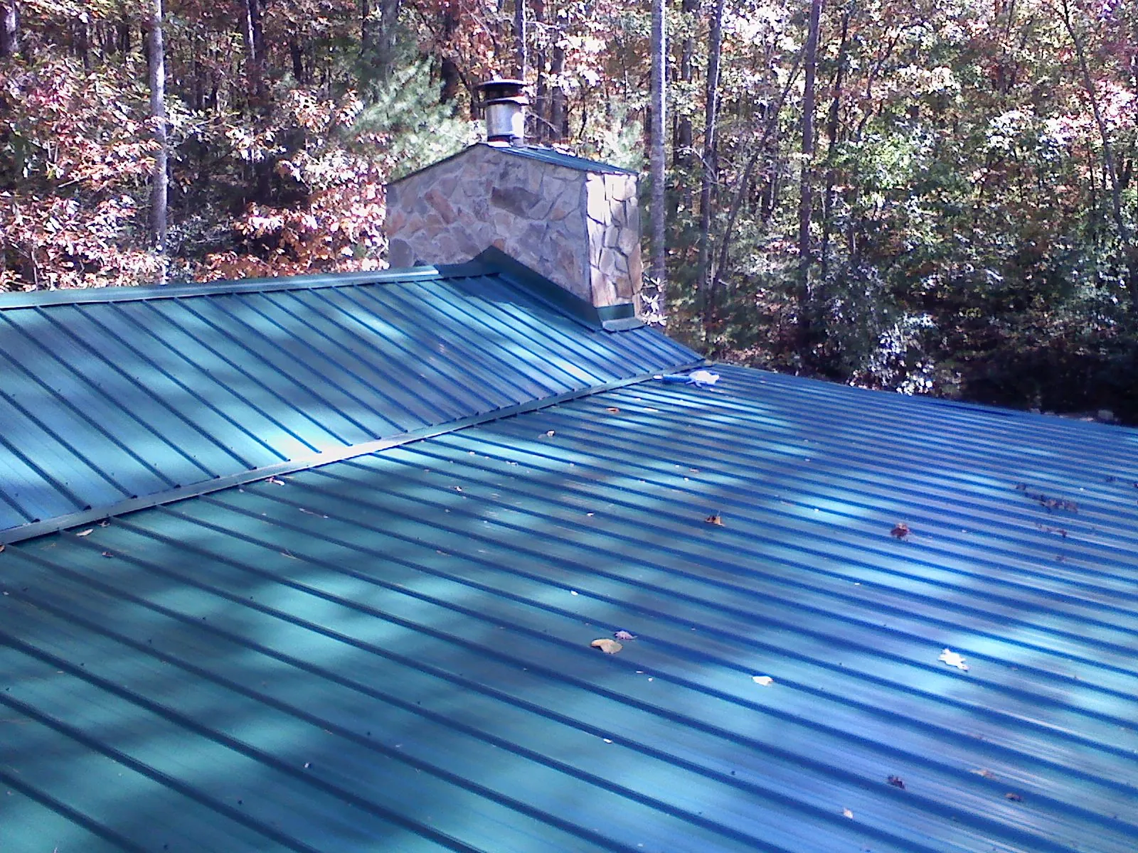 New green metal roof and stone chimney surrounded by autumn woods in East Dubuque