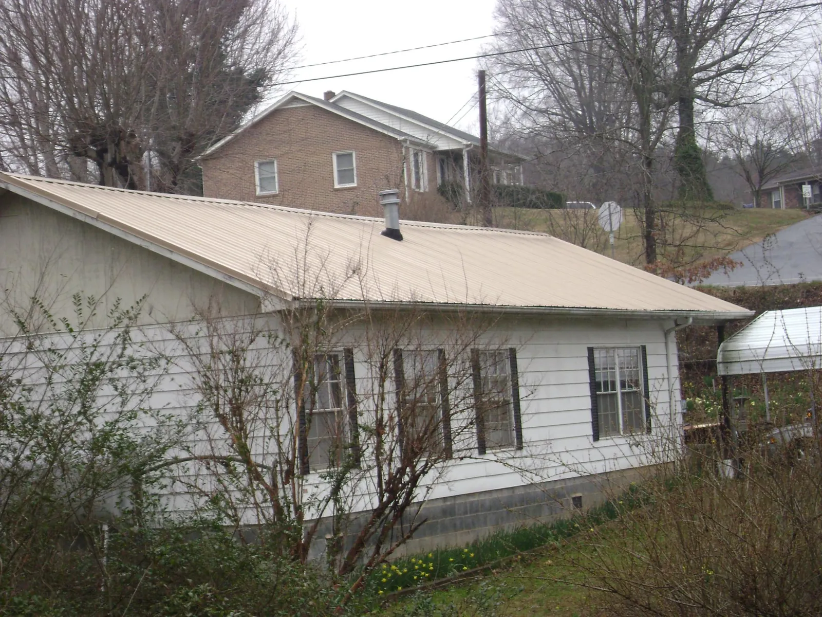 Tan metal roof on a white sided house set into a hillside — Commercial Roofing by Roofing Brothers in East Dubuque
